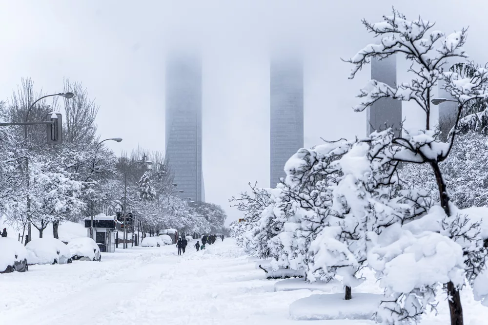 A beautiful shot of people walking in a snowy park with the Madrid four towers in the background