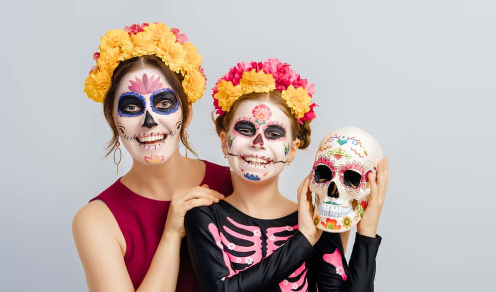 Adorable zombies in flower wreaths posing on white background. Happy family with Halloween creative makeup. Girls celebrating Mexican Day of the Dead.