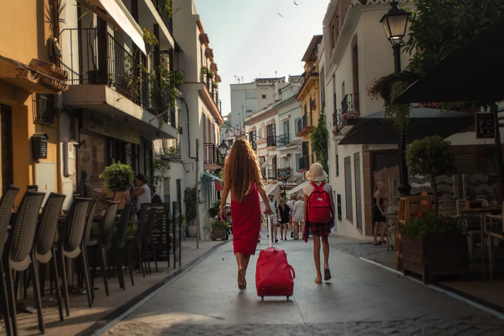 A woman carrying a suitcase while walking with her daughter down the street of Malaga, Spain