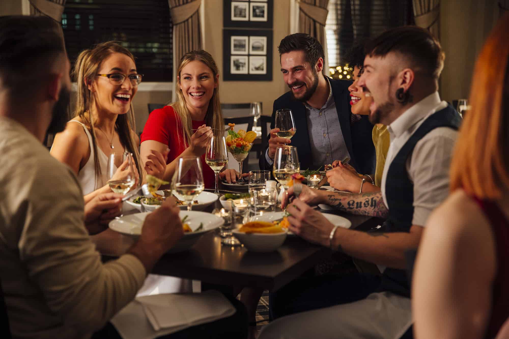 A group of friends are enjoying a meal together. They are talking and laughing while eating their starters and drinking champagne.
