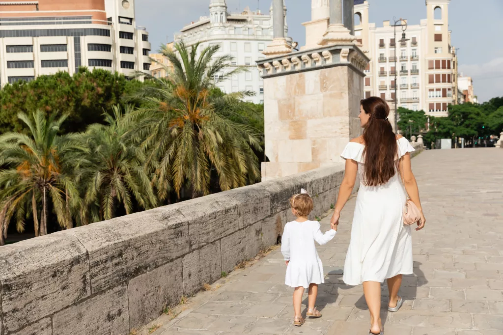 A woman in a white dress holding the hand of a kid while walking on the Puente Del Mar bridge in Valencia