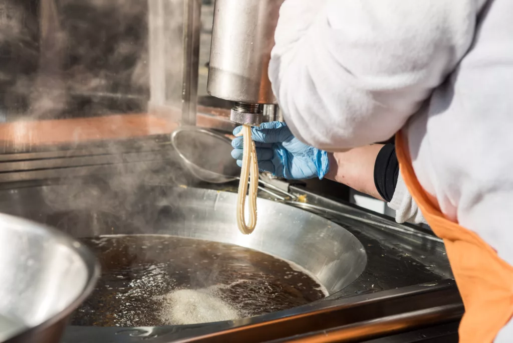 Close-up photograph of a person preparing the churro dough for cooking in the hot oil.