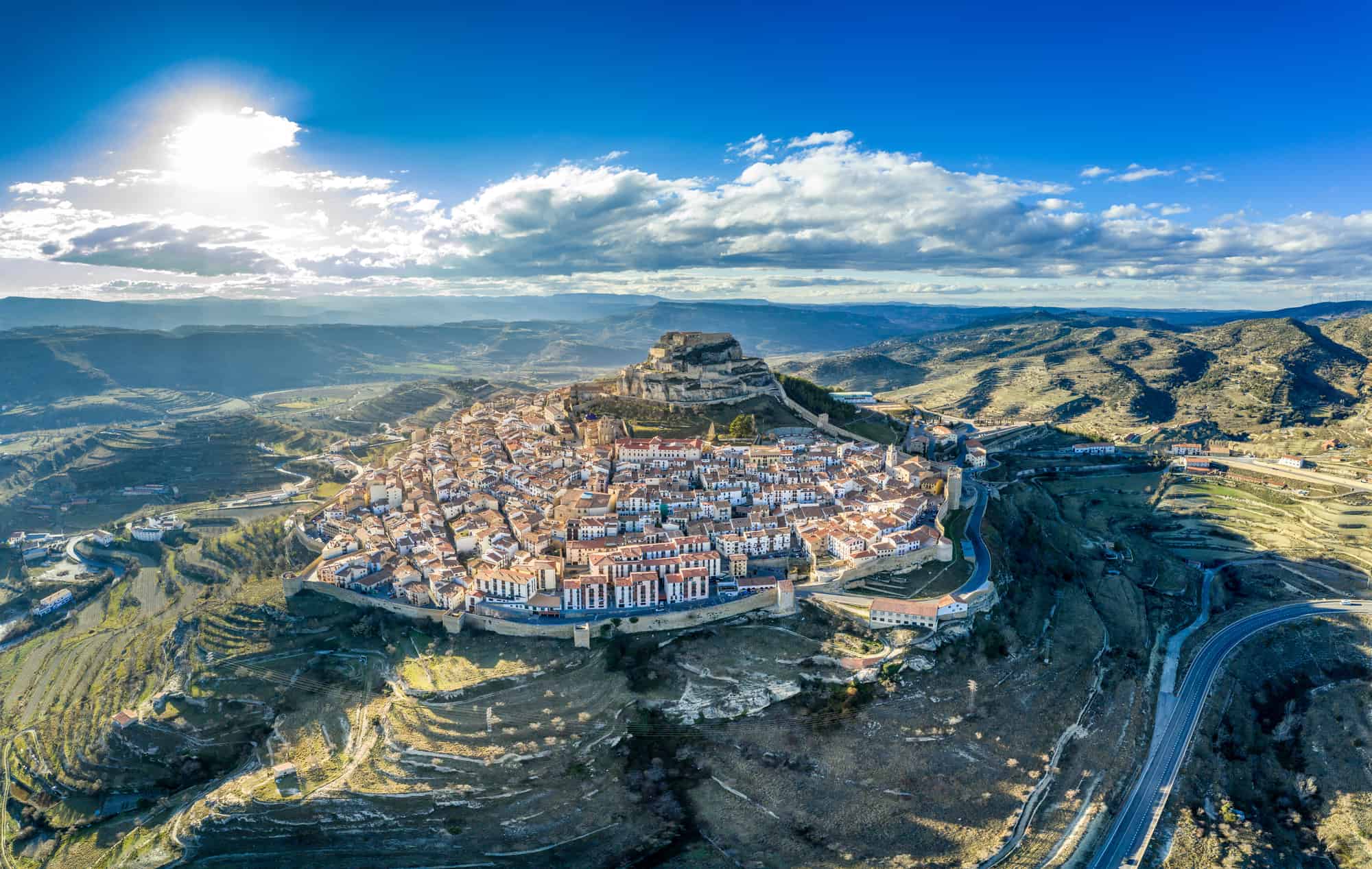 Aerial panoramic view of medieval walled Morella hilltop rampart and castle with blue sky in Spain