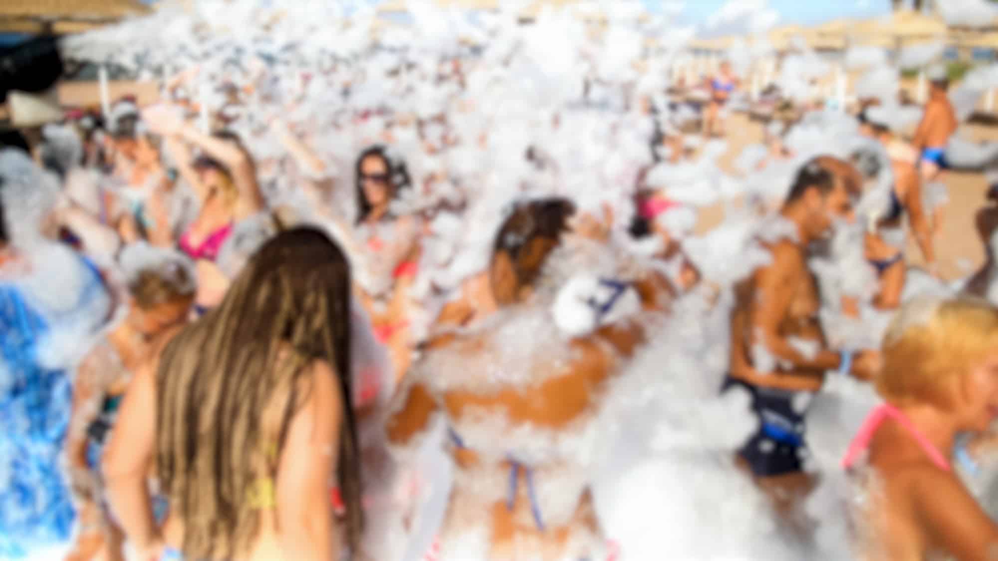 Happy cheerful crowd having fun on the soap foam disco party on the sandy sea beach of Gran Canaria, Spain