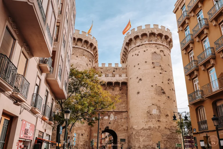Back view of Quart Towers in the El Carmen district of Valencia, with the right tower fully visible and the left partially obscured, both flying the Spanish flag—a historical must-see.