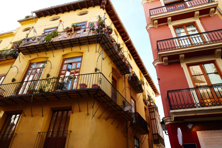 Looking up at two brightly colored buildings in yellow and red with beautiful balconies, capturing the vibrant architectural style typical of Valencia.