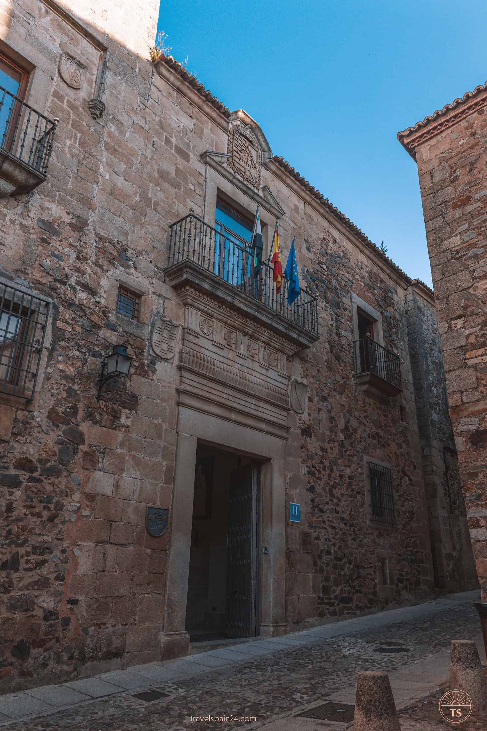 Entrance to Parador de Cáceres located in a quaint alley, marked by three flags fluttering above the doorway, welcoming visitors into the charm of Cáceres.