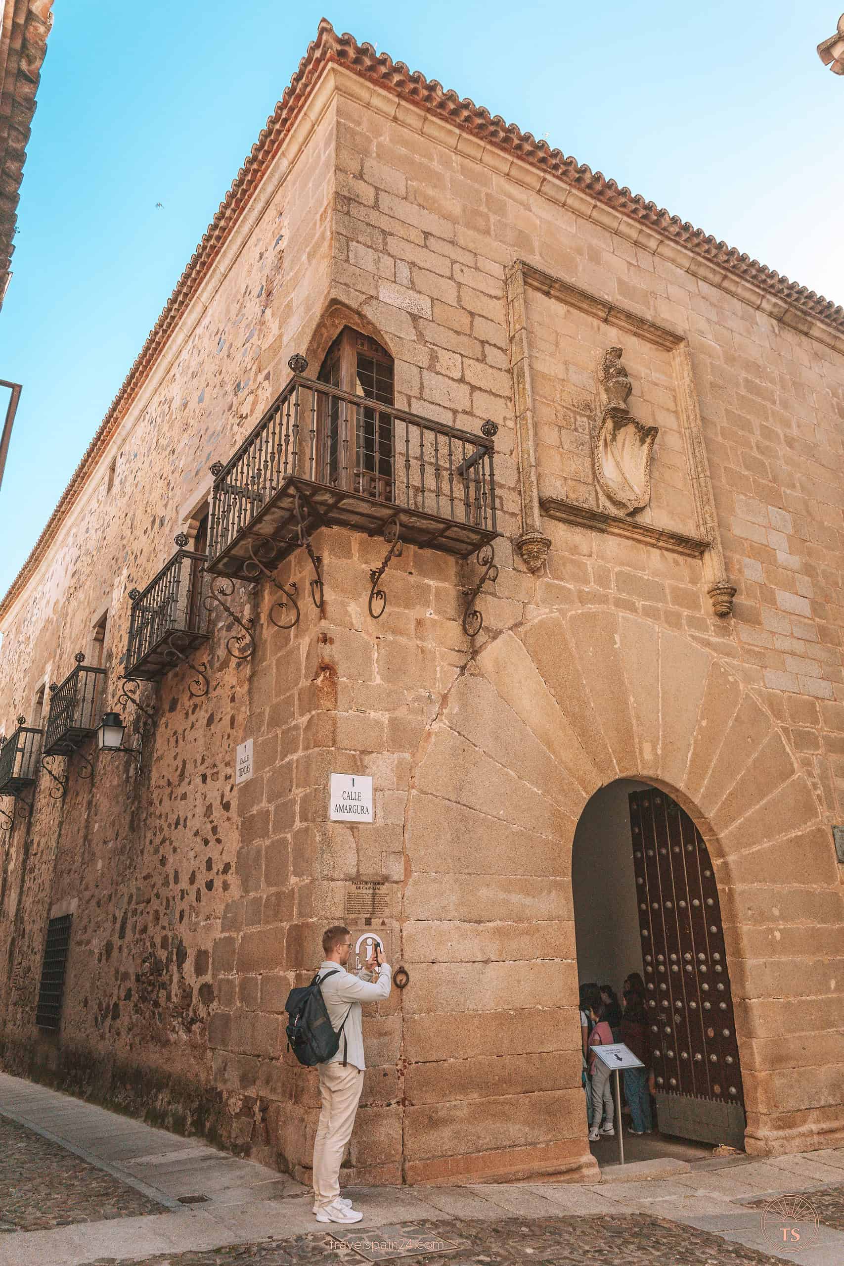 Timon van Basten at Casa del Mono o de los Cáceres-Nidos in Cáceres, capturing the scene next to a large arched entrance, with the street sign visible above.