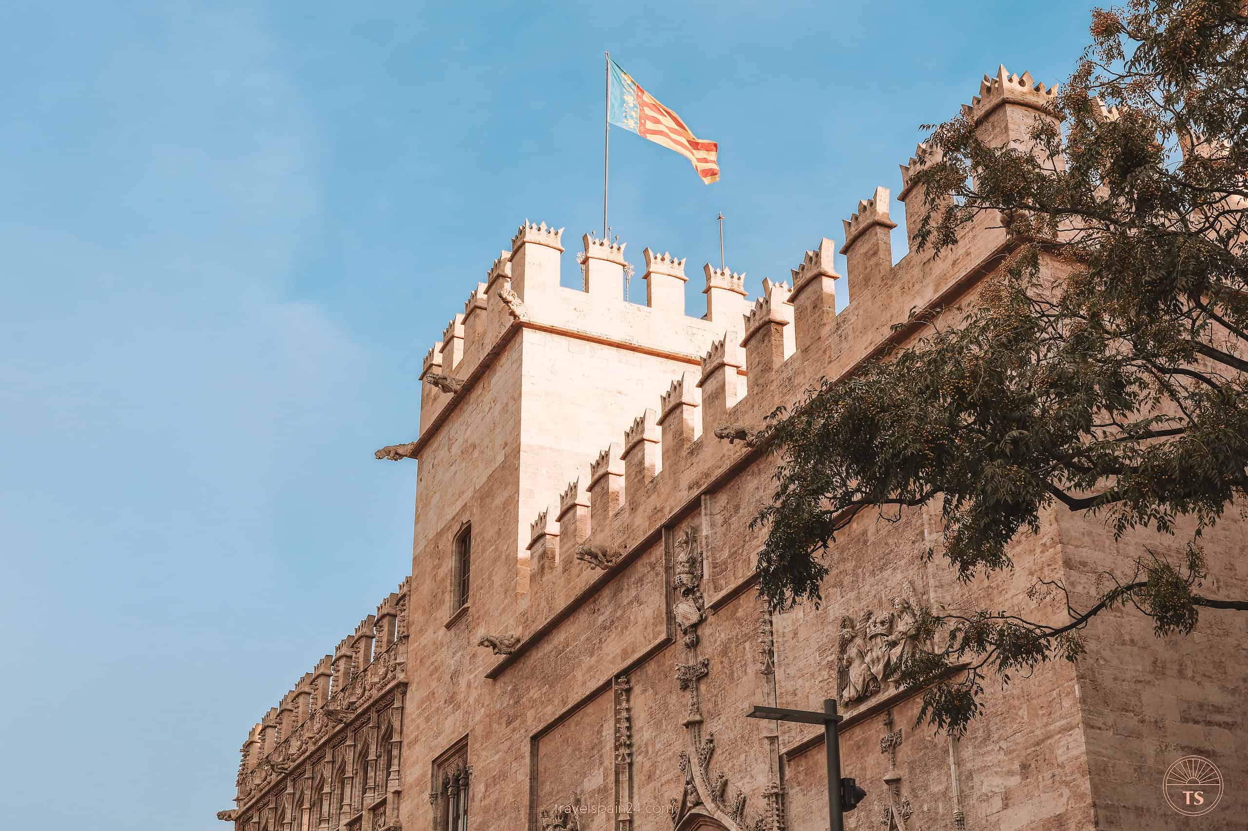 Front view of the iconic tower at La Lonja de la Seda in Valencia, with the Valencian flag proudly displayed on top, set against a bright blue sky