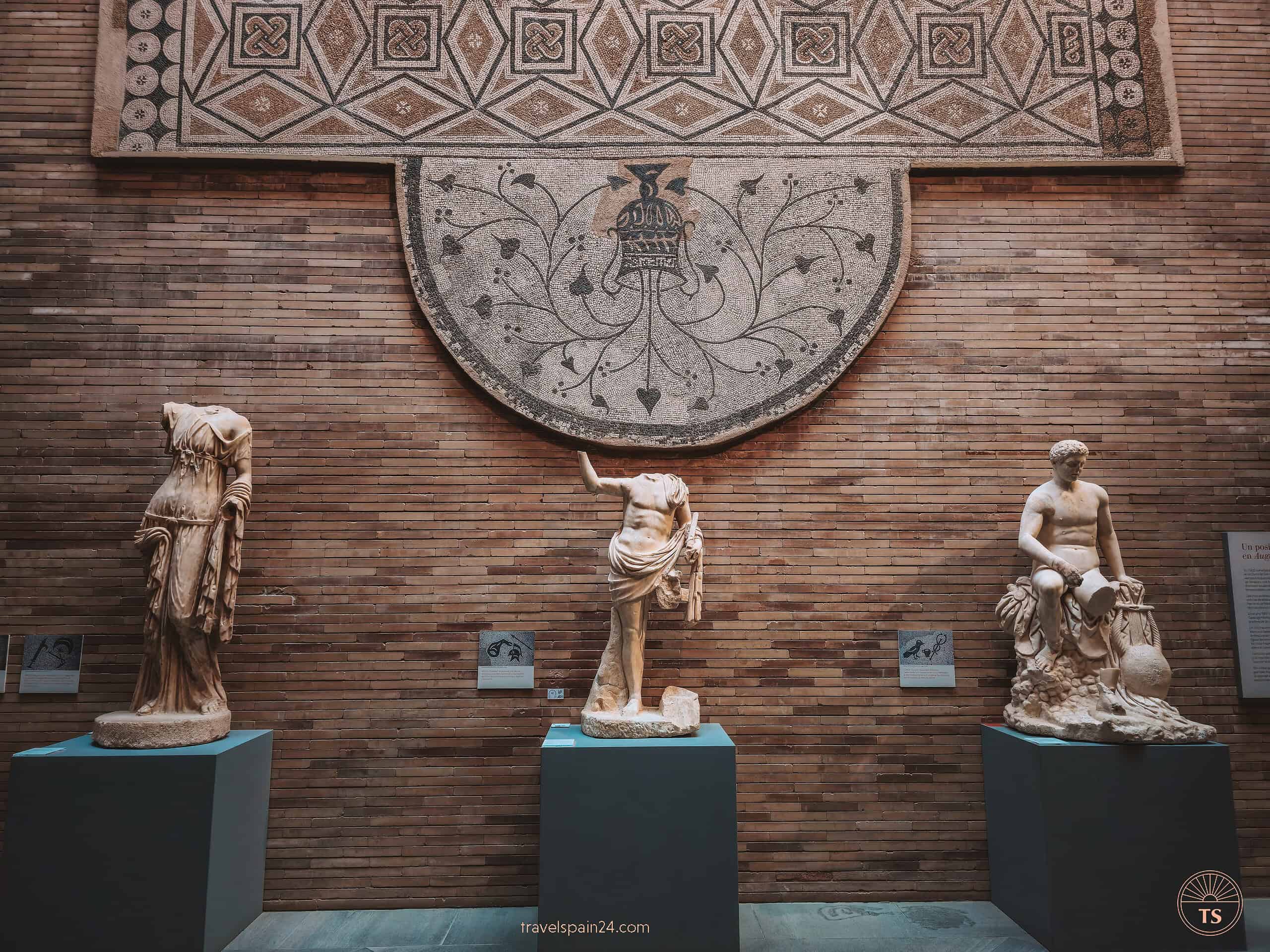 Three weathered statues and an ancient Roman mosaic floor displayed at the National Museum of Roman Art in Mérida, reflecting the city's deep archaeological heritage.