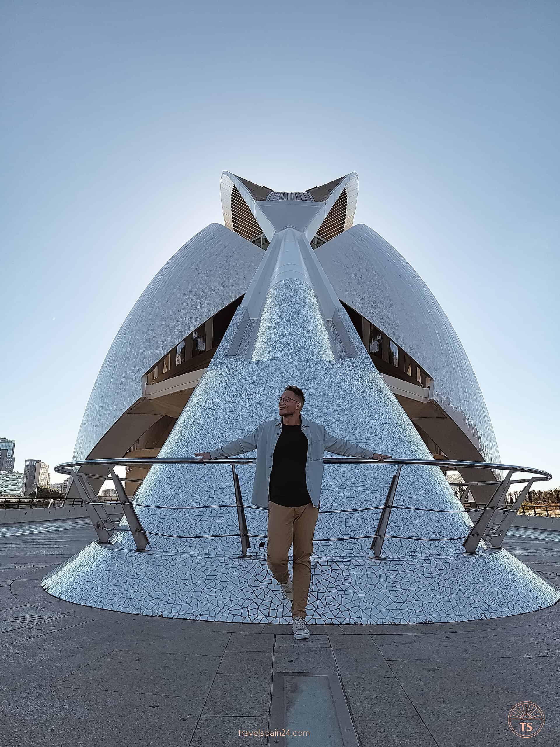 Timon van Basten posing in front of Palau de les Arts in Valencia's City of Arts and Sciences on a sunny day with clear blue skies, capturing the joyful essence of visiting this iconic site.