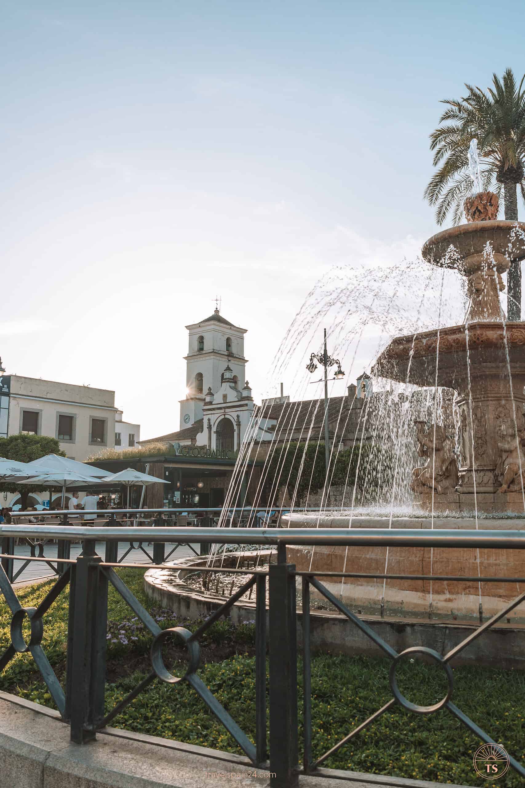 The fountain at Plaza España in Mérida, with sunlight casting rays behind the Co-cathedral of Saint Mary Major, highlighting a serene day in the city.