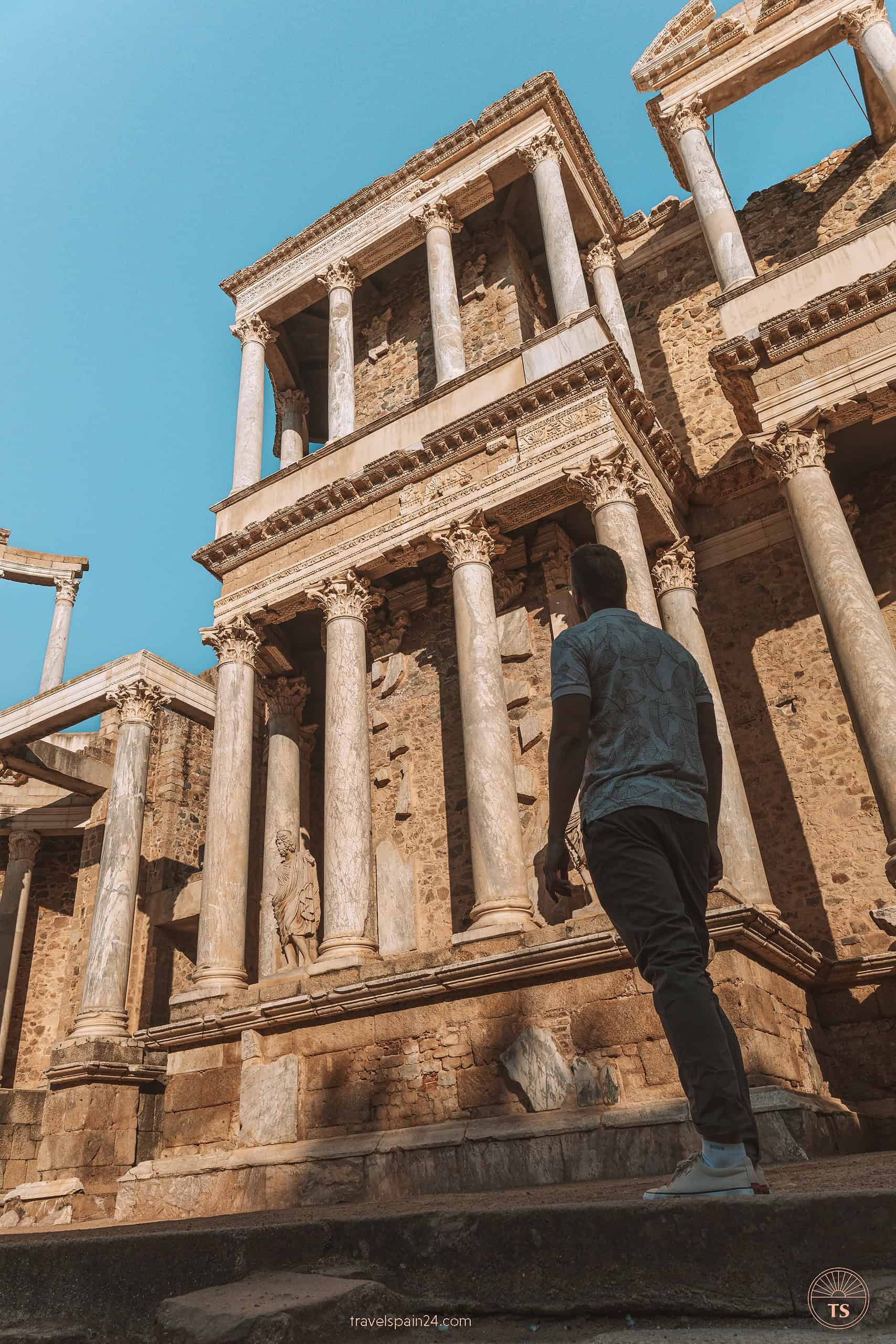 Timon van Basten admiring the Roman Theatre in Mérida, with sunlight highlighting the ancient pillars against a clear blue sky.
