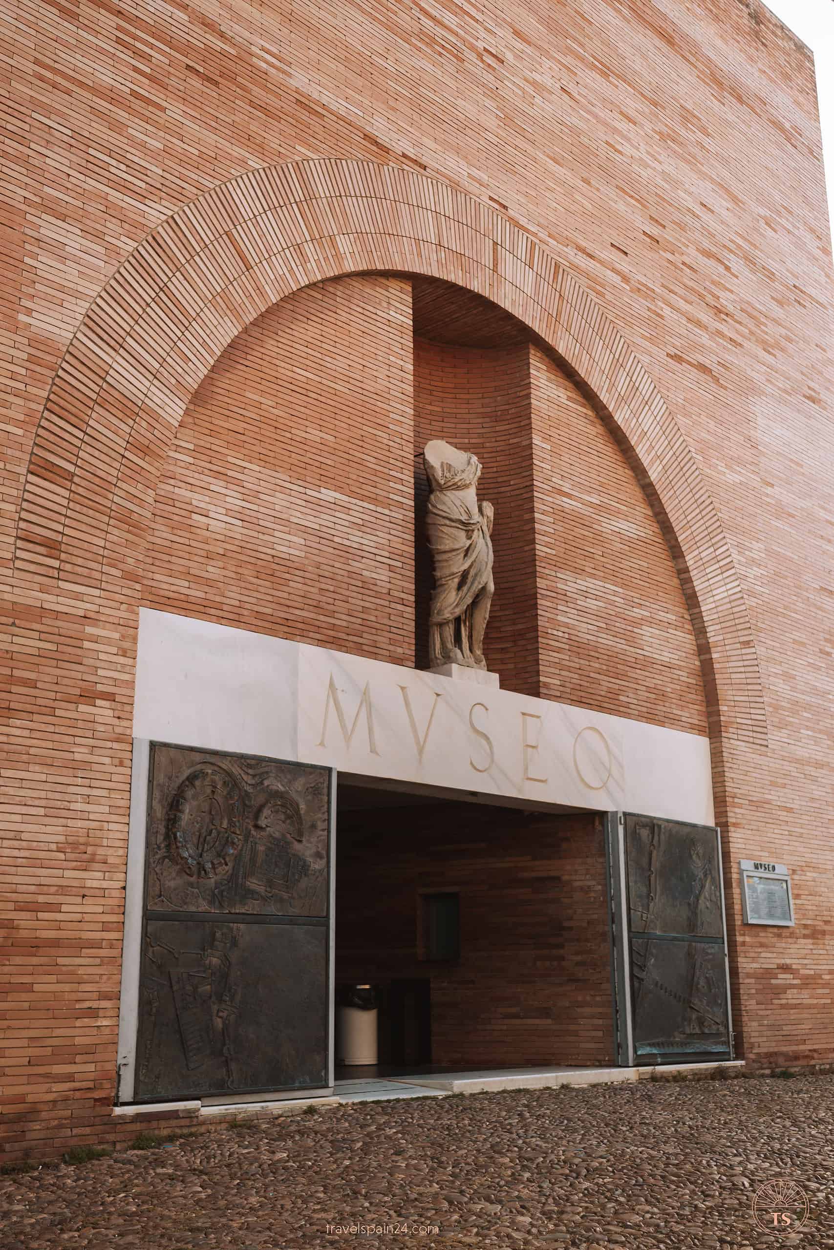 Entrance of the National Museum of Roman Art in Mérida, framed by an arched brick entryway and an ancient Roman statue, inviting visitors to explore further.