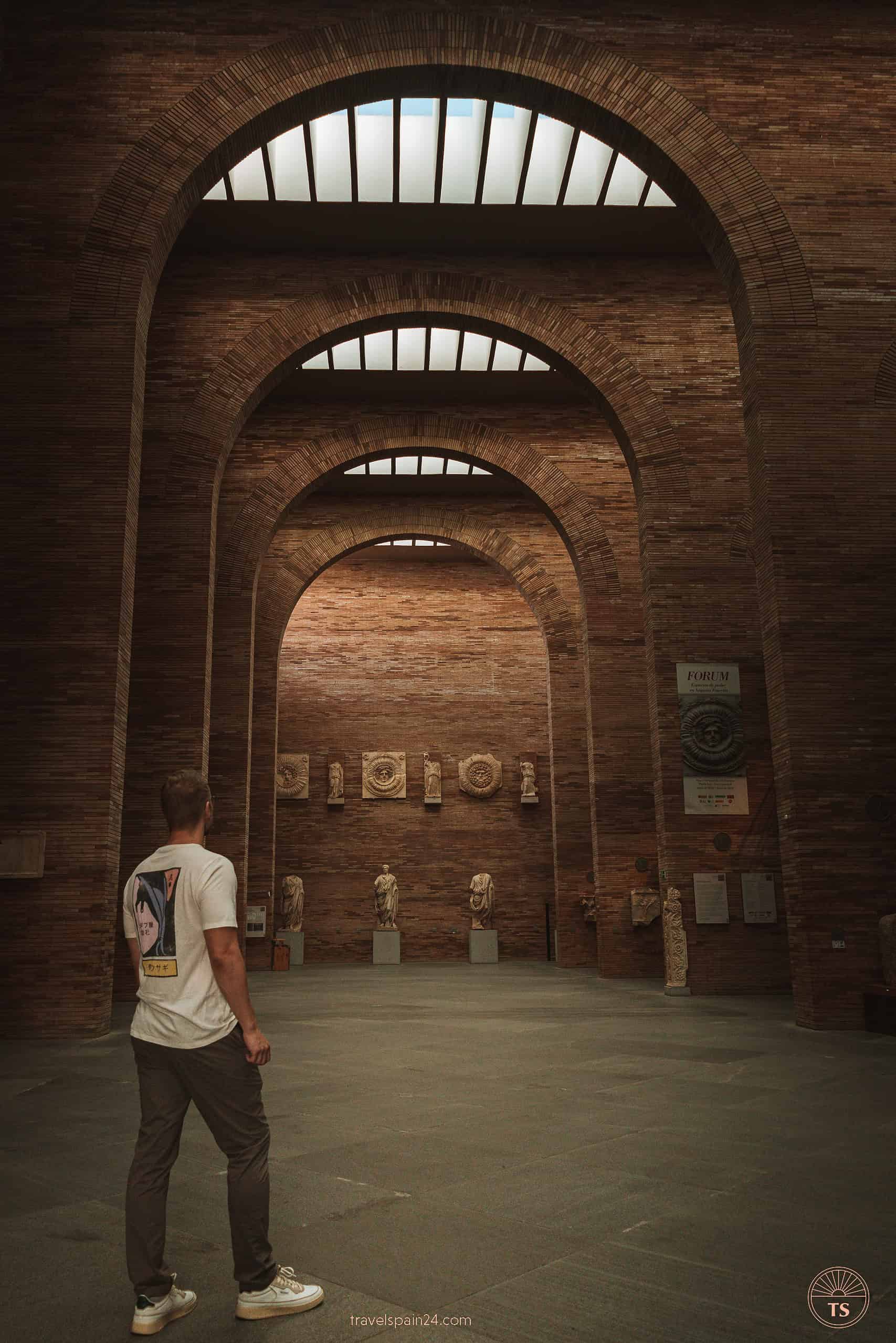 Timon van Basten inside the National Museum of Roman Art in Mérida, walking towards a collection of ancient Roman statues, flanked by tall arched brick entrances.