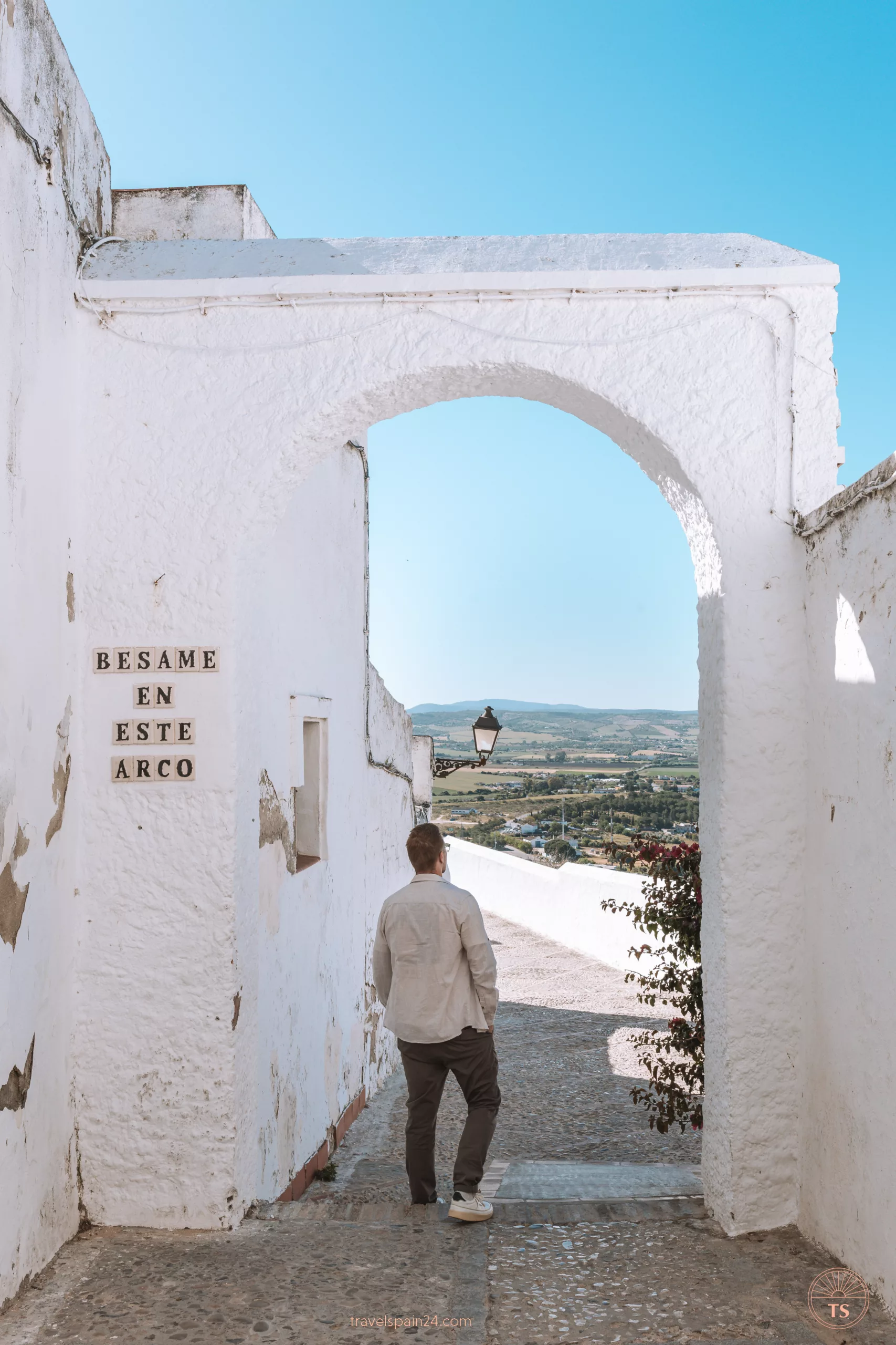 Timon van Basten stands casually under the 'Bésame en Este Arco' Instagram arch in Arcos de la Frontera, looking away at the panoramic view.