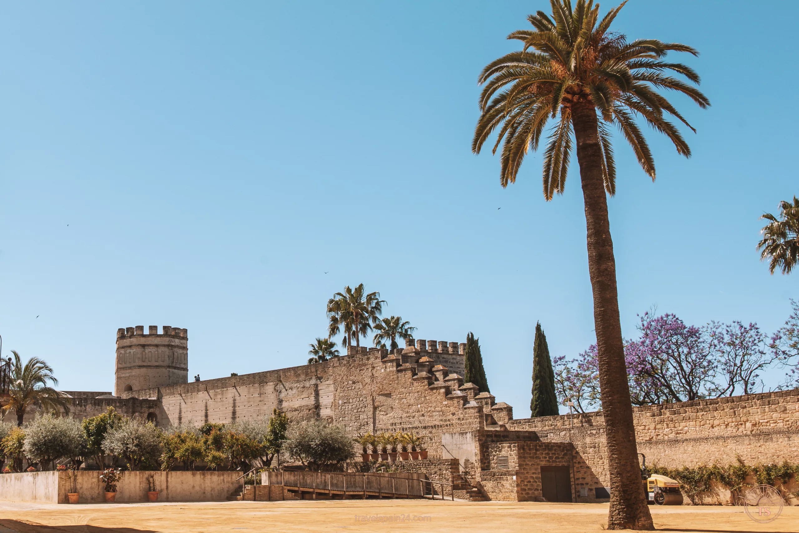 Front view of the Alcazar in Jerez de la Frontera, showing the tower, walls, and part of the garden on a sunny morning. This image highlights the historical significance of the Alcazar in Jerez.