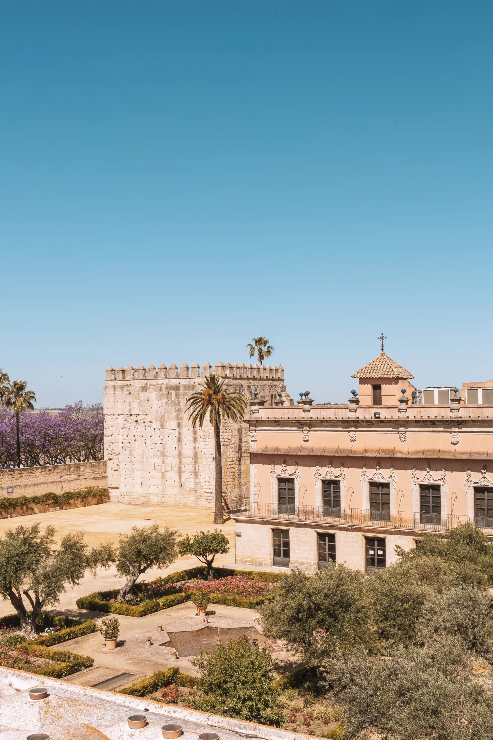 View from the walls of the Alcazar in Jerez de la Frontera, showing the gardens and fountain on a sunny day. This image showcases the Alcazar's beautiful grounds.