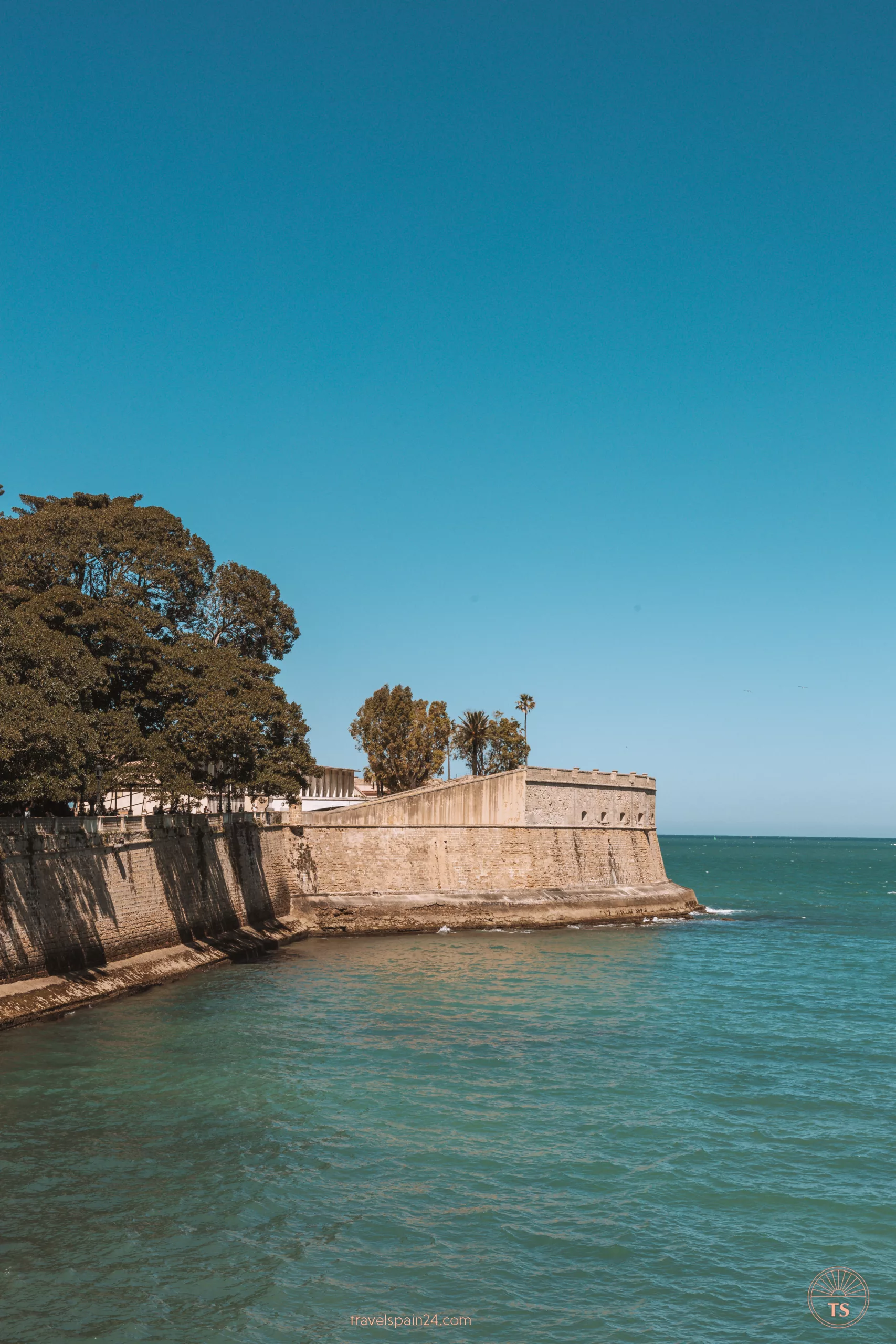 Exterior view of Baluarte de Cadiz, with sunlight illuminating its walls and waves crashing against it. This image captures the beauty of Cadiz's coastal fortification.
